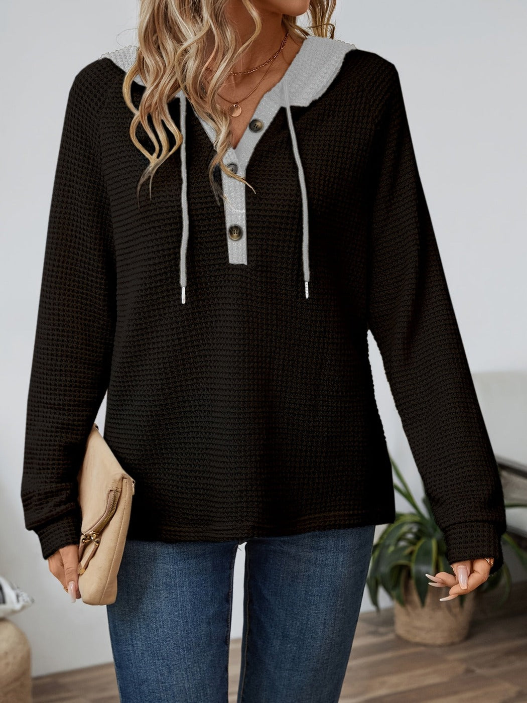 Vrouw in een wafelhoodie in Zwart/Grijs met grijze knoopsluiting en een clutch | Boutique Moda