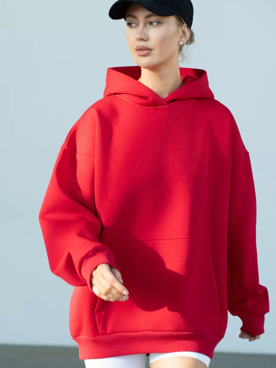 Vrouw met een zwarte pet in een rode hoodie, tijdens het wandelen | Boutique Moda