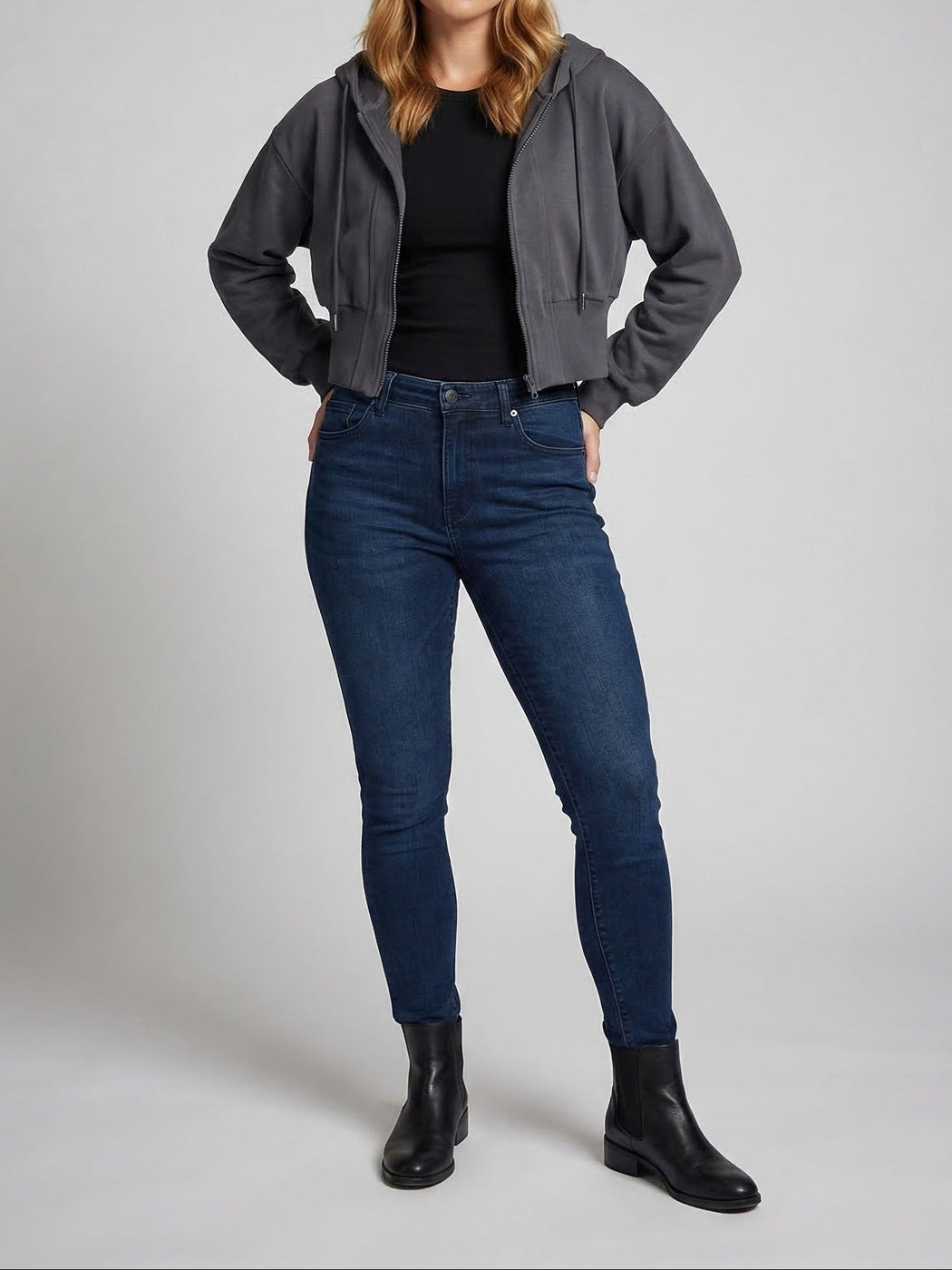 Vrouw in een open donkergrijs kort vest over een zwart topje, met een donkere jeans en enkellaarsjes | Boutique Moda