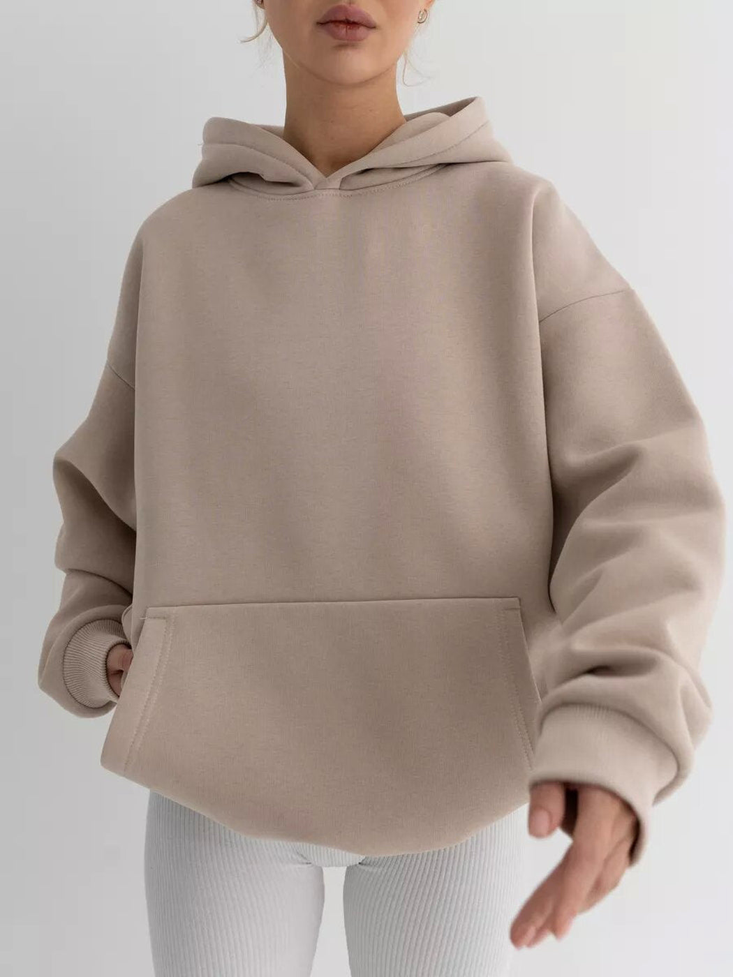 Vrouw in een taupe hoodie met een witte legging, hand in de zak | Boutique Moda