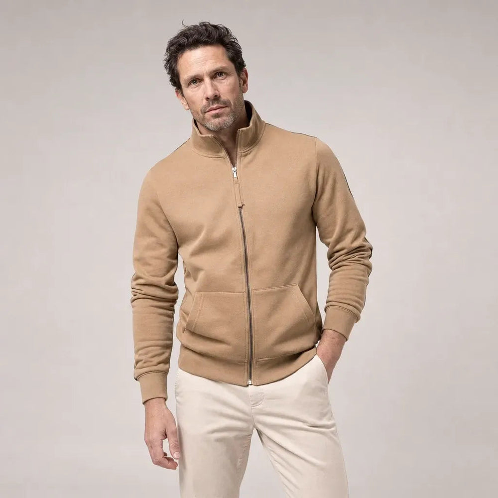 Man in een camelkleurig sweatvest met een crèmekleurige broek, met een hand in zijn broekzak | Boutique Moda