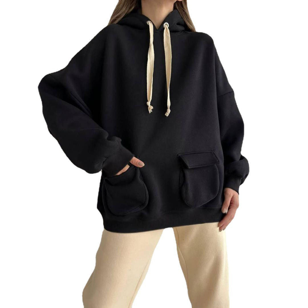 Vrouw in een zwarte oversized hoodie met lichte koorden en een lichte broek, hand in de zak | Boutique Moda