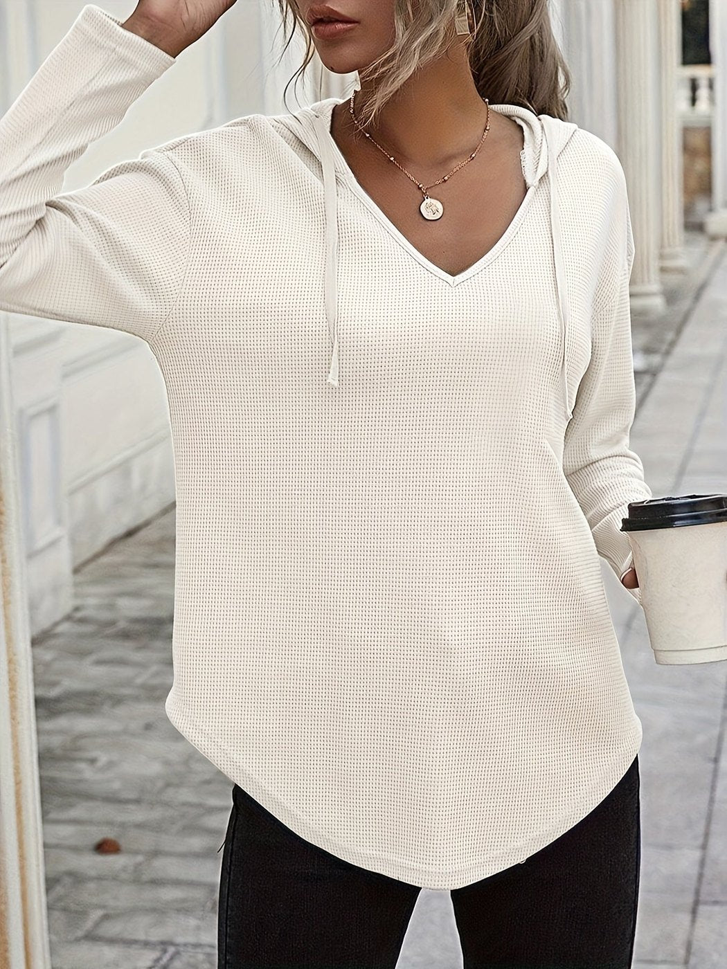 Vrouw in een gebroken witte hoodie met dun koord in een lichte straat, hand in het haar | Boutique Moda