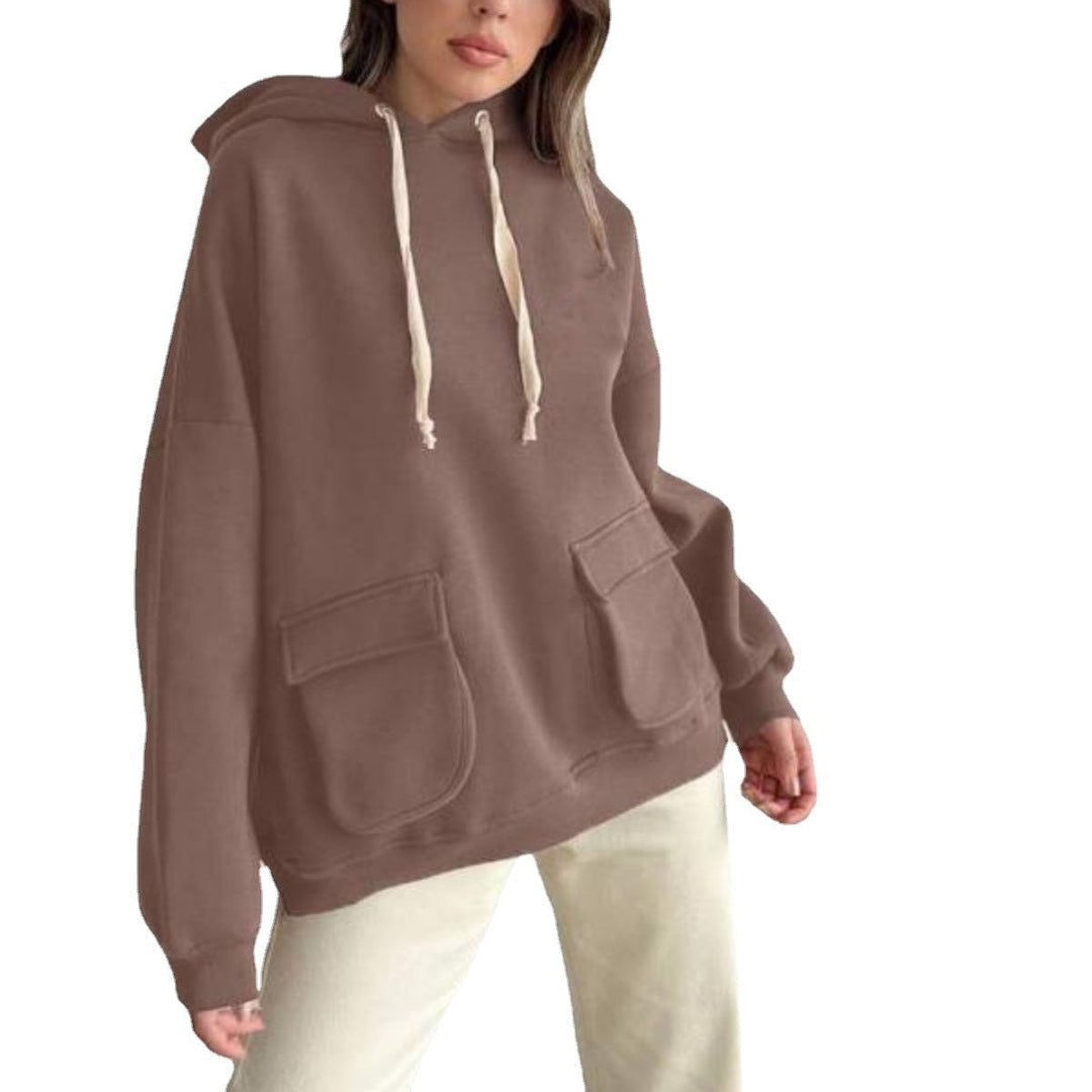 Vrouw in een mokkakleurige oversized hoodie met klepzakken en een lichte broek, op een witte achtergrond | Boutique Moda