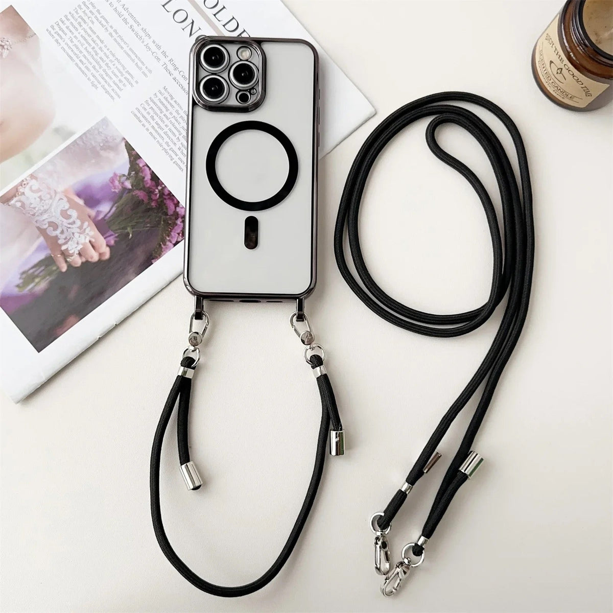 Transparant iPhone-hoesje met zwart koord, plat neergelegd naast tijdschrift | Boutique Moda