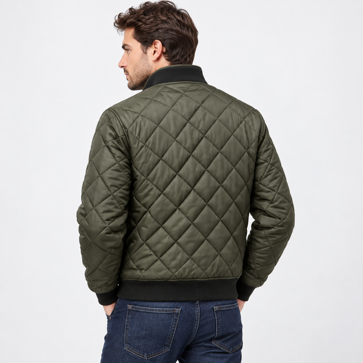 A man seen from behind wearing an olive green quilted diamond-pattern bomber jacket with a black ribbed collar, cuffs and hem, paired with dark jeans.
