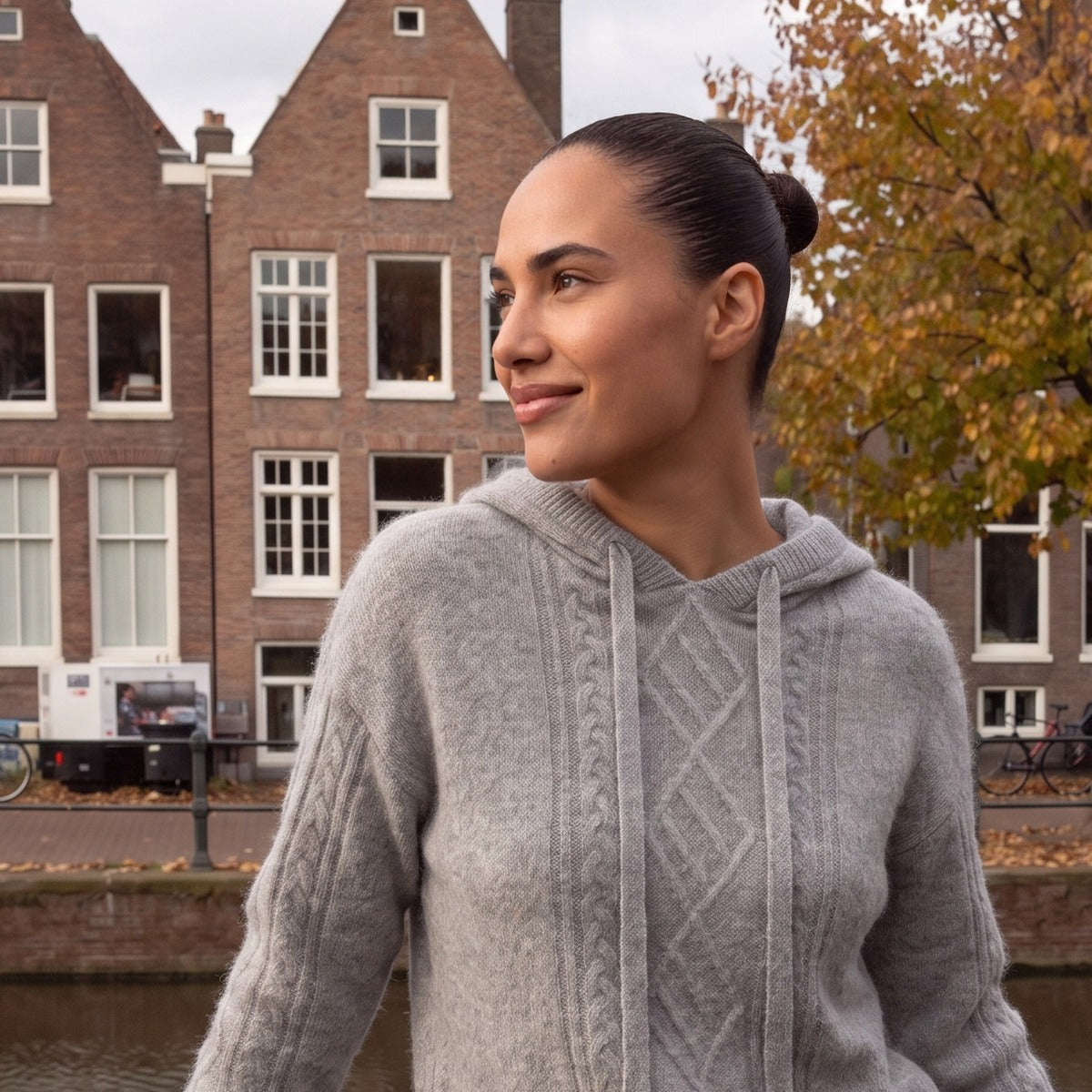 Gebreide hoodie met kabelpatroon in grijs, gedragen aan een Nederlandse gracht