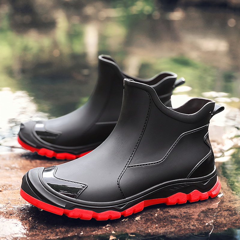 A pair of black ankle boots with red soles sitting on a wet rock near water.