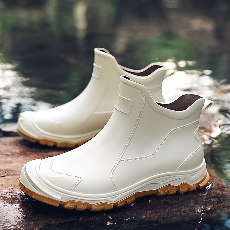 A pair of cream colored rain boots with tan soles displayed on wet rocks near water.