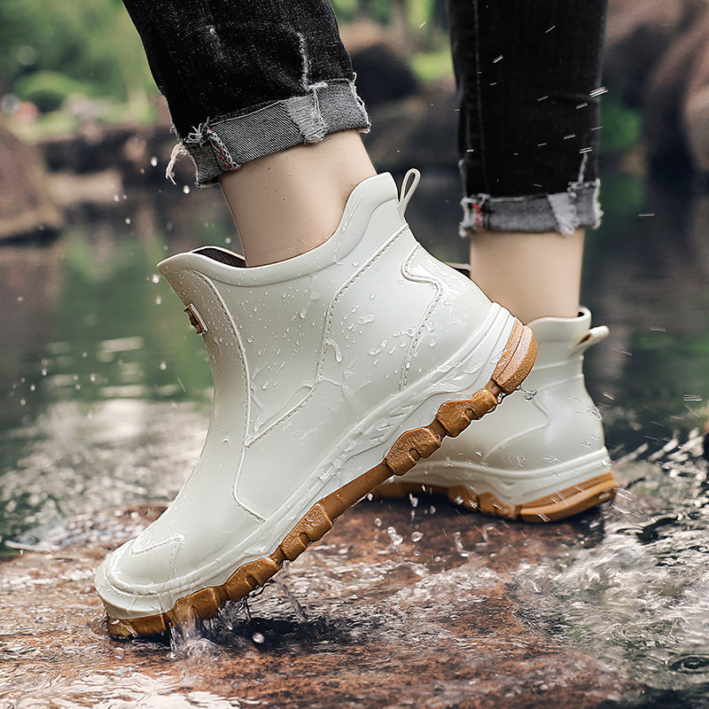 A person wearing cropped jeans steps through a puddle in white rain boots with tan treaded soles.