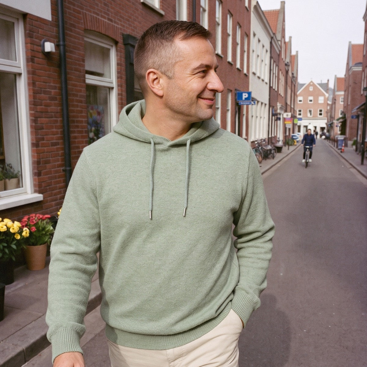 Gebreide hoodie voor heren in saliegroen, gedragen in een straat in Utrecht