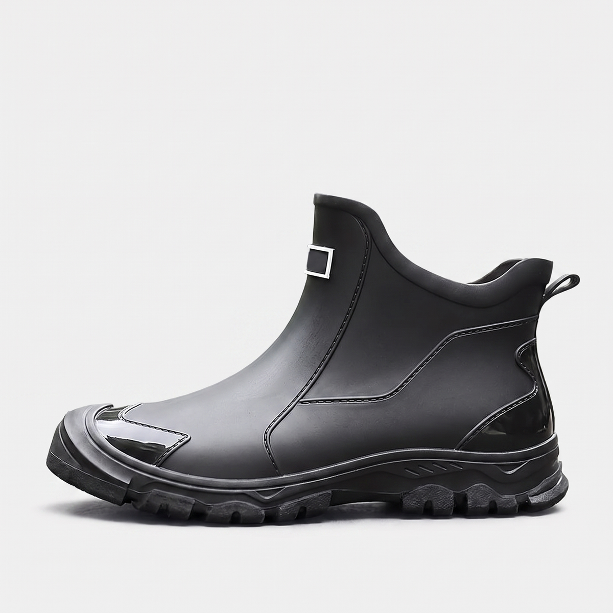A black rubber ankle boot with chunky lugged sole and a small metal buckle tab, shown against a plain white background.