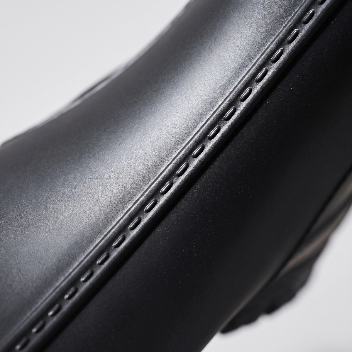 A close-up of a black boot showing stitched detailing along the welt and part of the lugged sole.