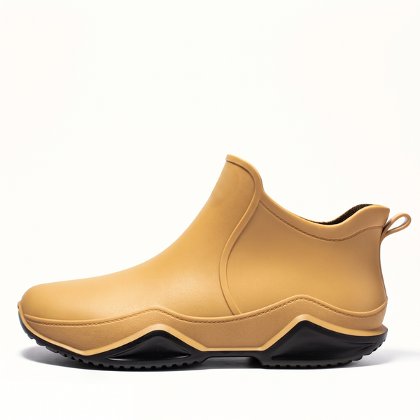 Side profile studio shot of a mustard yellow rubber ankle rain boot with a black wavy sole and a rear pull tab on a white background.
