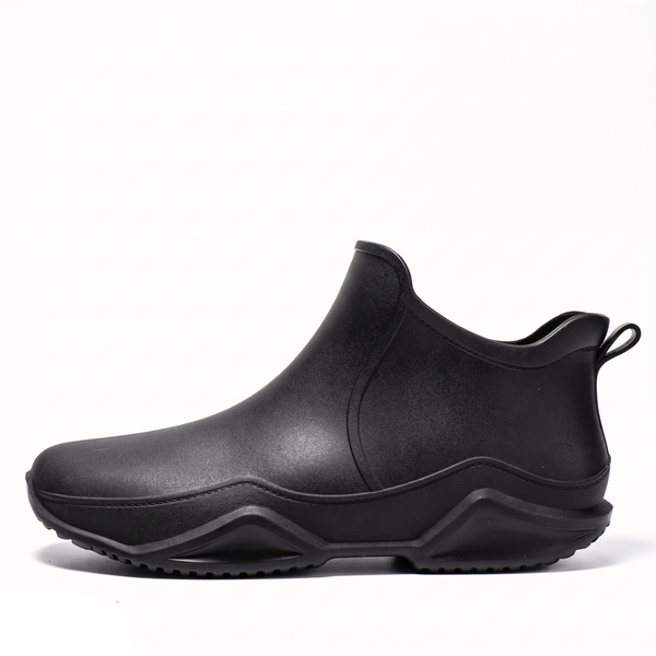Side profile of a black ankle-height rubber rain boot with a chunky wavy sole and a rear pull loop, on a plain white background.