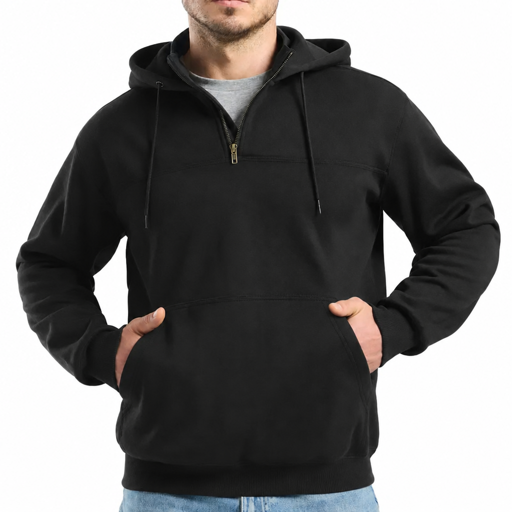 A man wears a black half zip hoodie with a kangaroo pocket and drawstrings, hands in pockets.