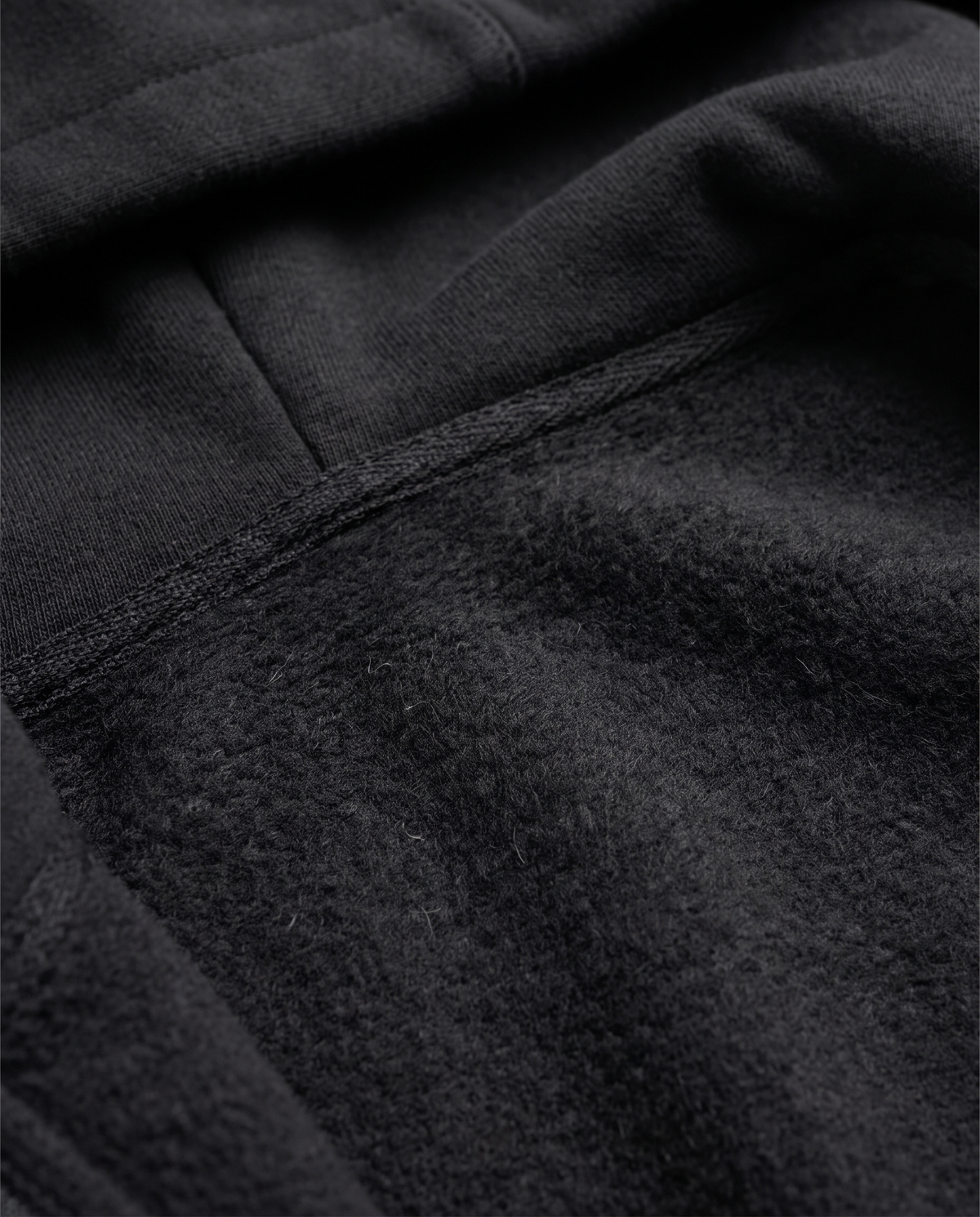 A man seen from behind wearing a black zip-up hoodie with the hood up, paired with blue jeans, close-up view