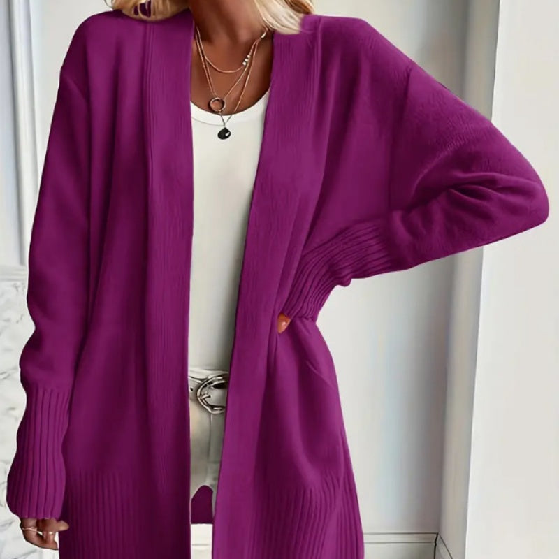 A woman wears a long open purple ribbed-cuff cardigan over a white top and layered necklaces.