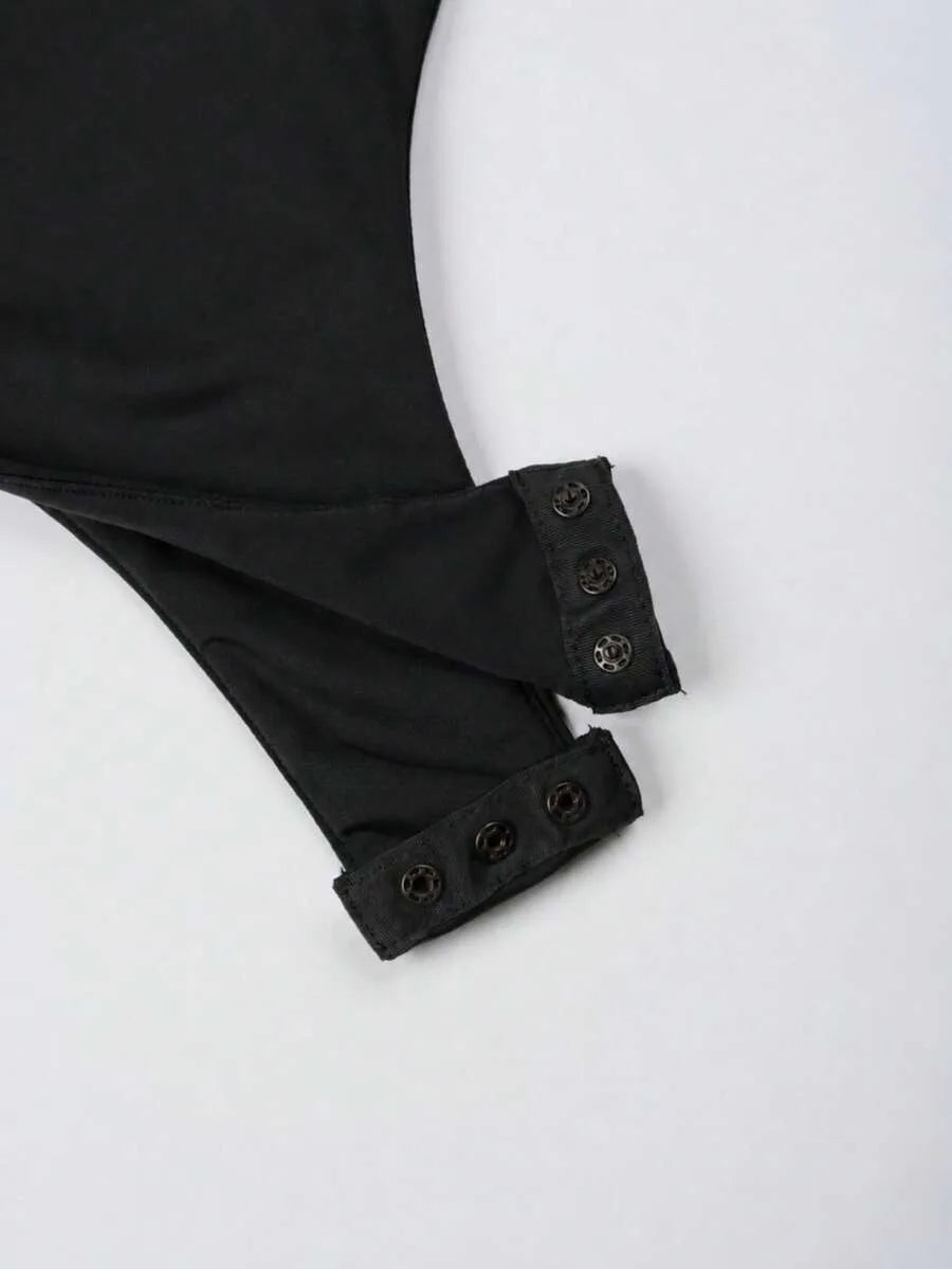 Close up of a black garment's sleeve cuffs with snap button closures on a grey surface.