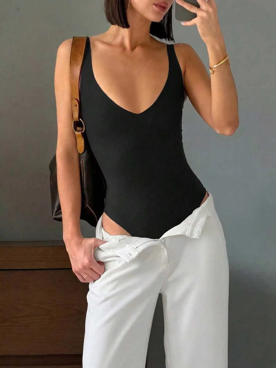 A woman wears a black deep V-neck bodysuit tucked into white trousers while holding a phone and a brown handbag.