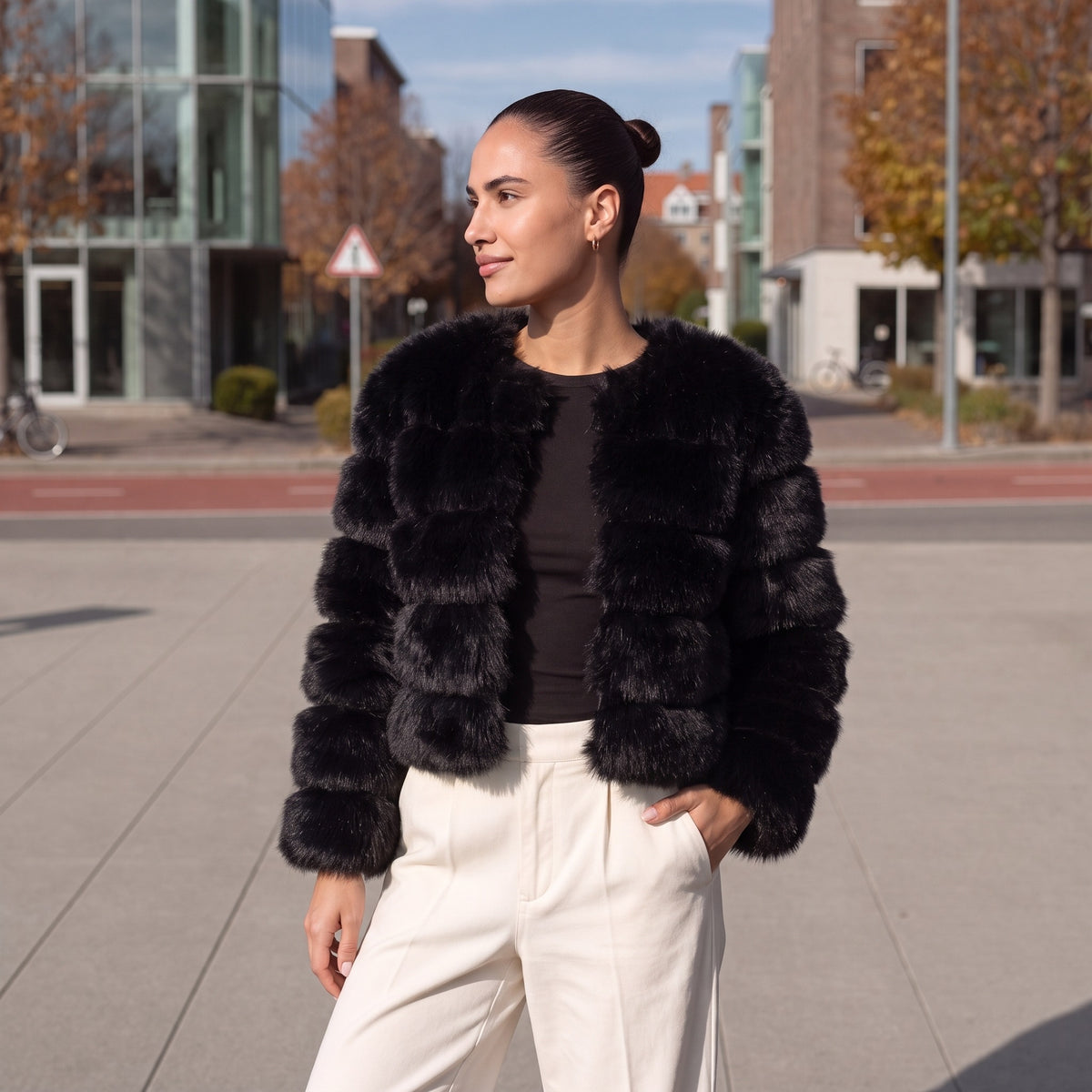 Vrouw draagt zwart kort fluffy imitatiebont jasje met witte broek buiten | Boutique Moda