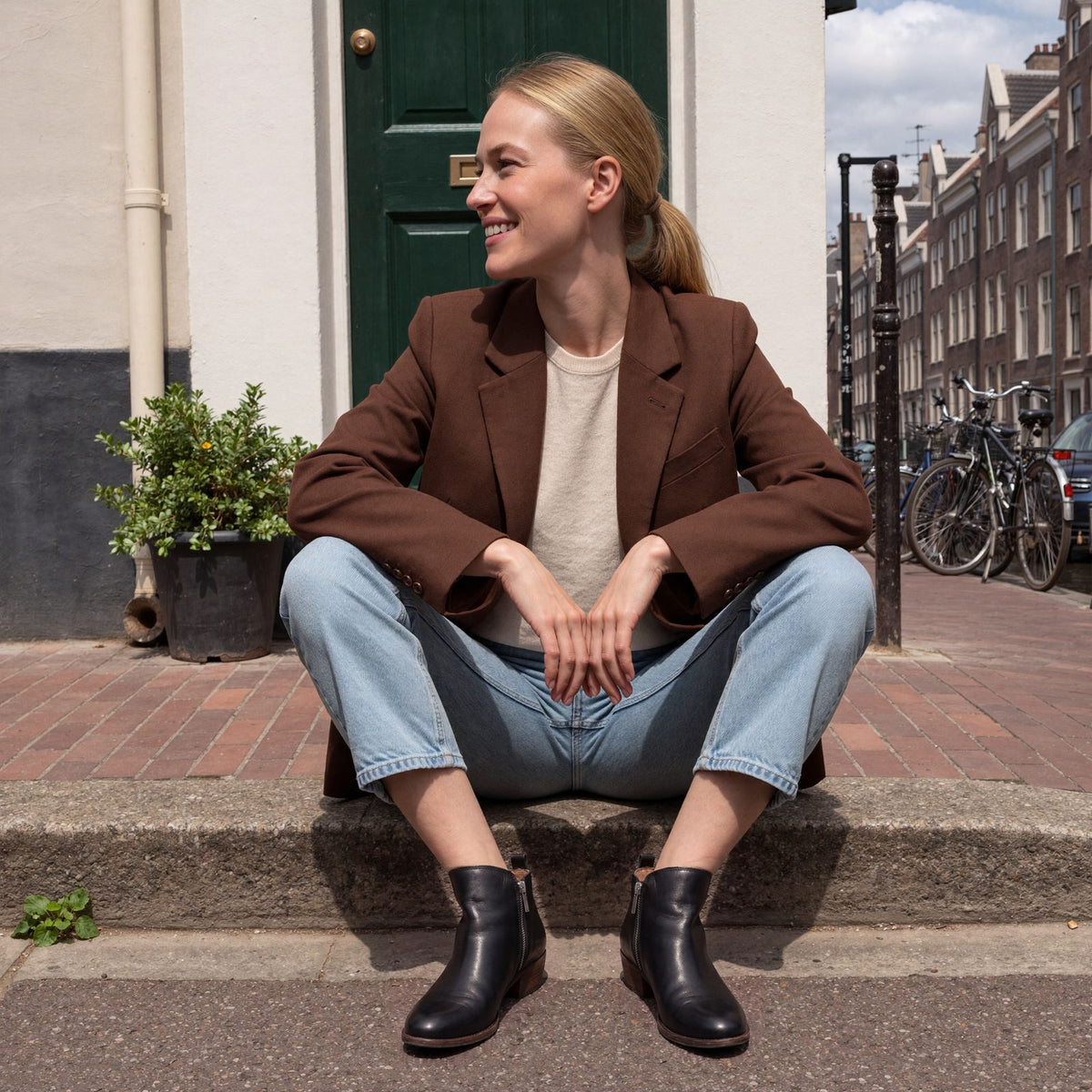 Vrouw draagt zwarte enkellaarzen met blokhak en ritssluiting, zittend op de stoep van een grachtenpand in Amsterdam | Boutique Moda