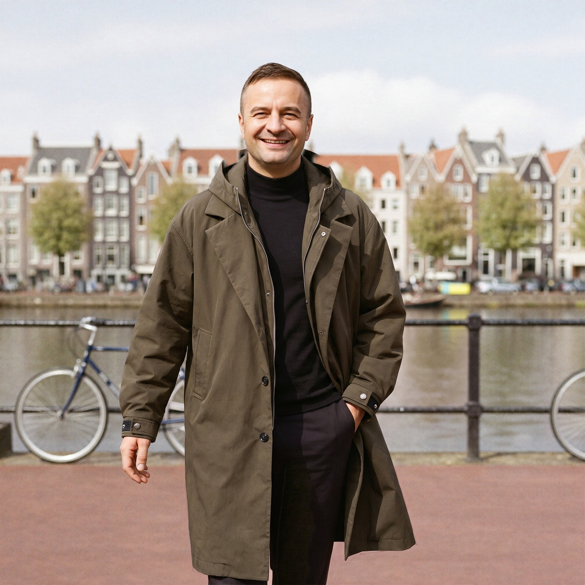 Lange regenjas voor heren in khaki, gedragen langs een Amsterdamse gracht