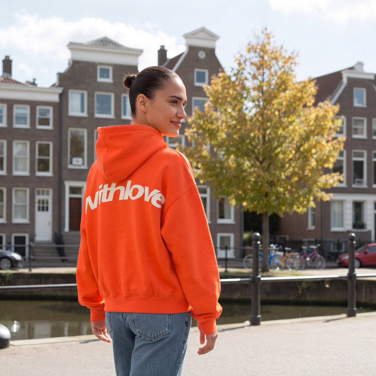 Amira draagt de oranje oversized hoodie met grote rugprint in een grachtenstraat in Utrecht | Boutique Moda