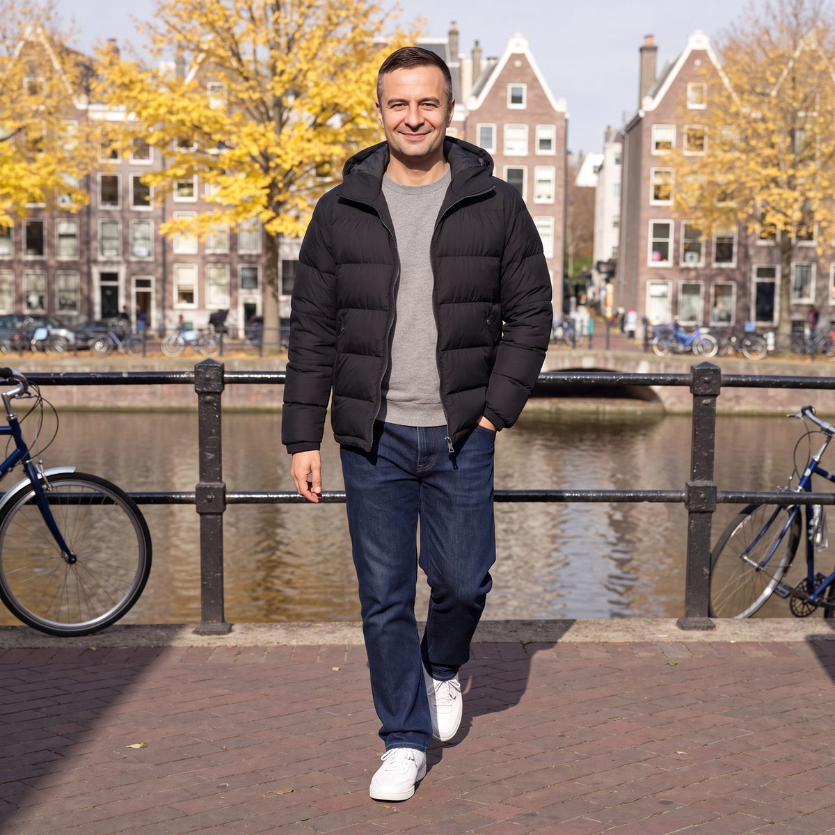 Man draagt zwarte pufferjas met capuchon open over een grijze trui, wandelend langs een Amsterdamse gracht | Boutique Moda