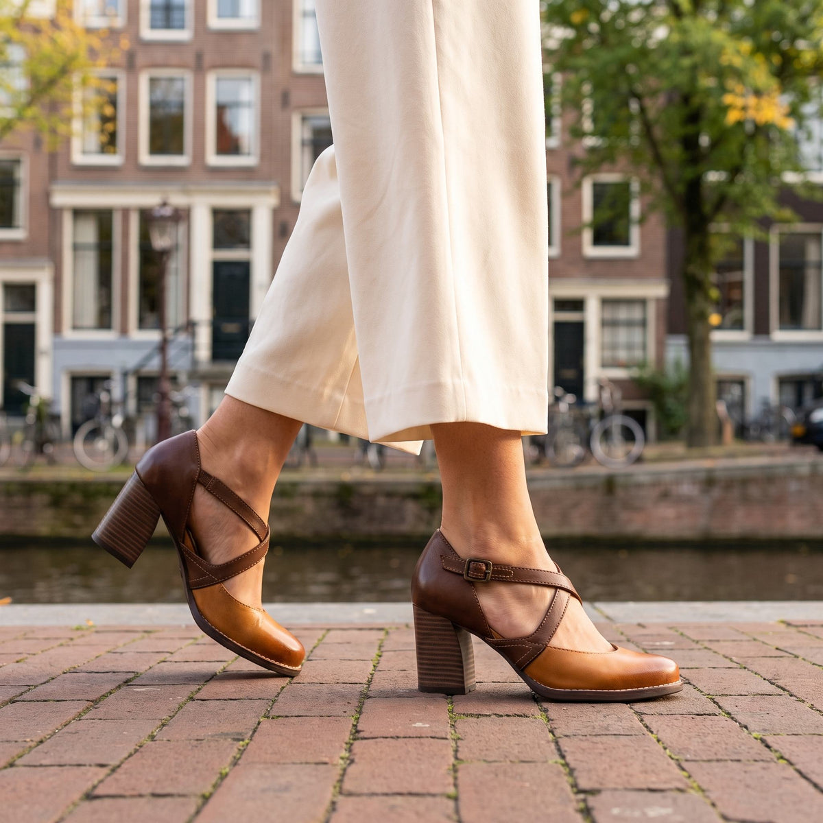 Bruine pumps met blokhak en gekruiste bandjes, gedragen met een crème wijde broek aan een Amsterdamse gracht | Boutique Moda