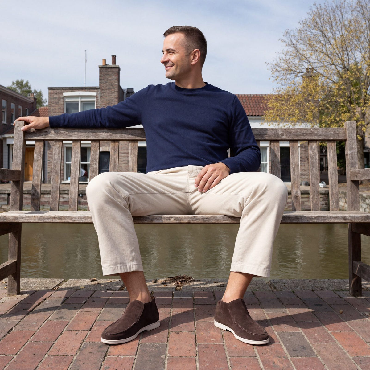 Man draagt donkerbruine suède loafers met witte zool, zittend op een bankje aan de gracht in Utrecht | Boutique Moda