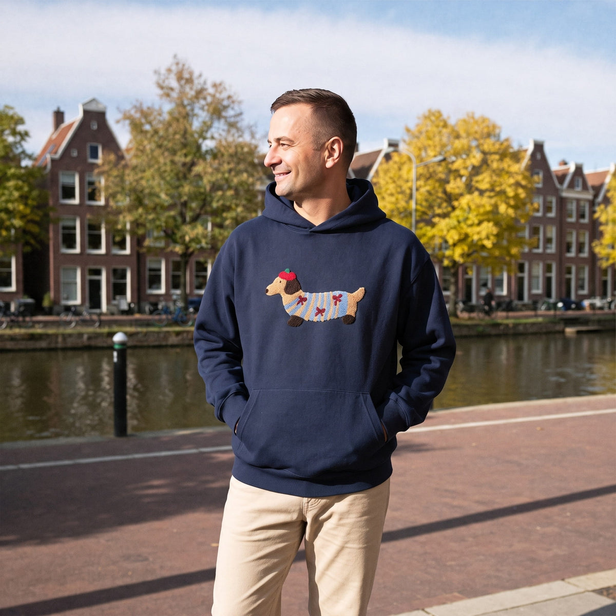 Man draagt marineblauwe hoodie met geborduurd teckelhondje bij grachtenpand | Boutique Moda