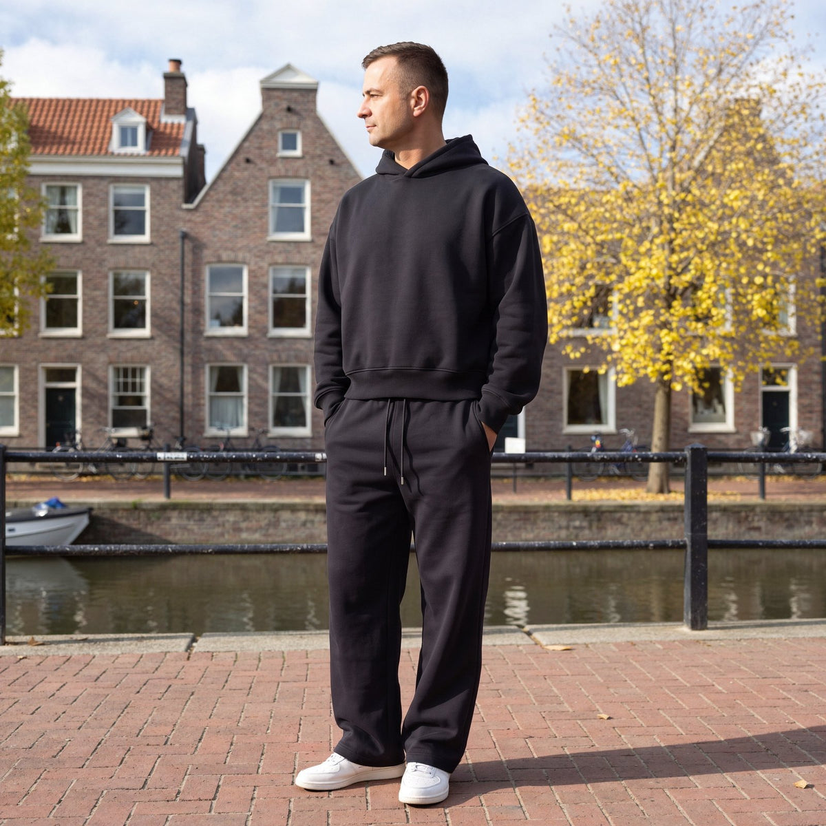 Man draagt zwart trainingspak met oversized hoodie en wijde joggingbroek aan een gracht in Utrecht | Boutique Moda
