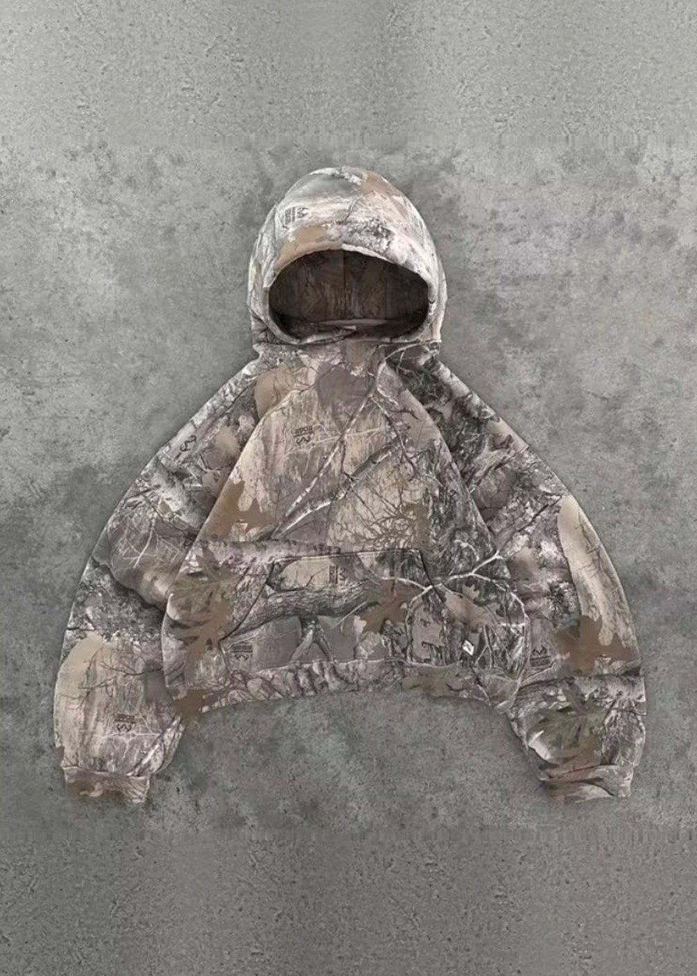 Beige camouflage oversized hoodie met capuchon, plat neergelegd op betonnen ondergrond | Boutique Moda
