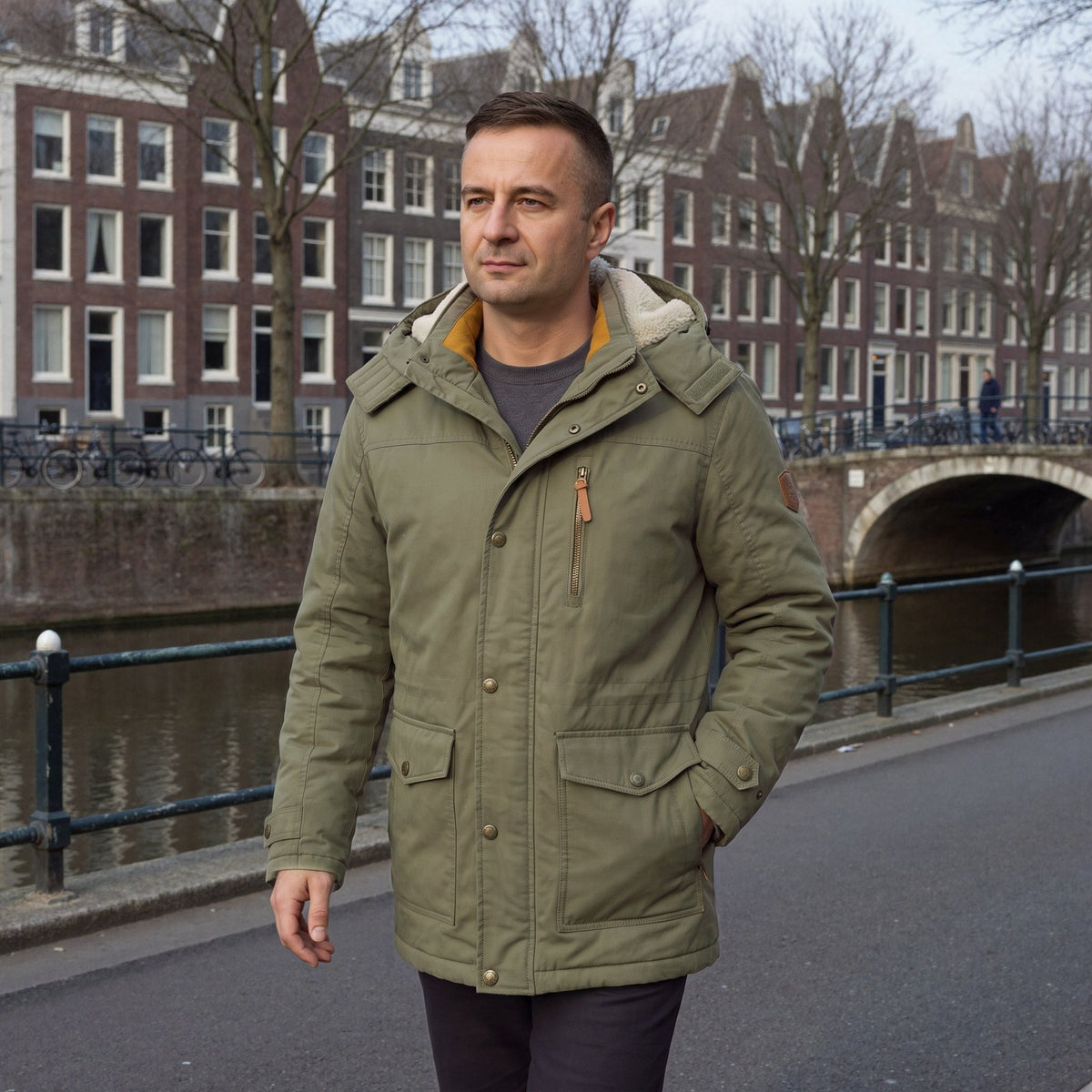Man draagt kaki winterparka met fleecevoering langs een gracht in Amsterdam | Boutique Moda