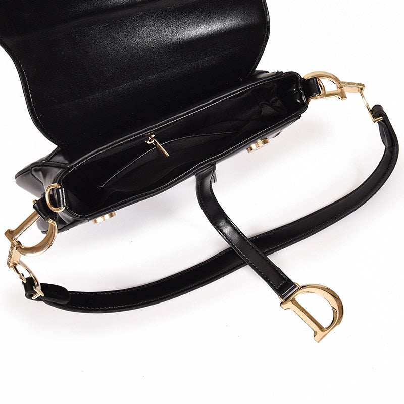 Zwarte imitatieleren schoudertas met gouden gespen, plat gefotografeerd close-up | Boutique Moda