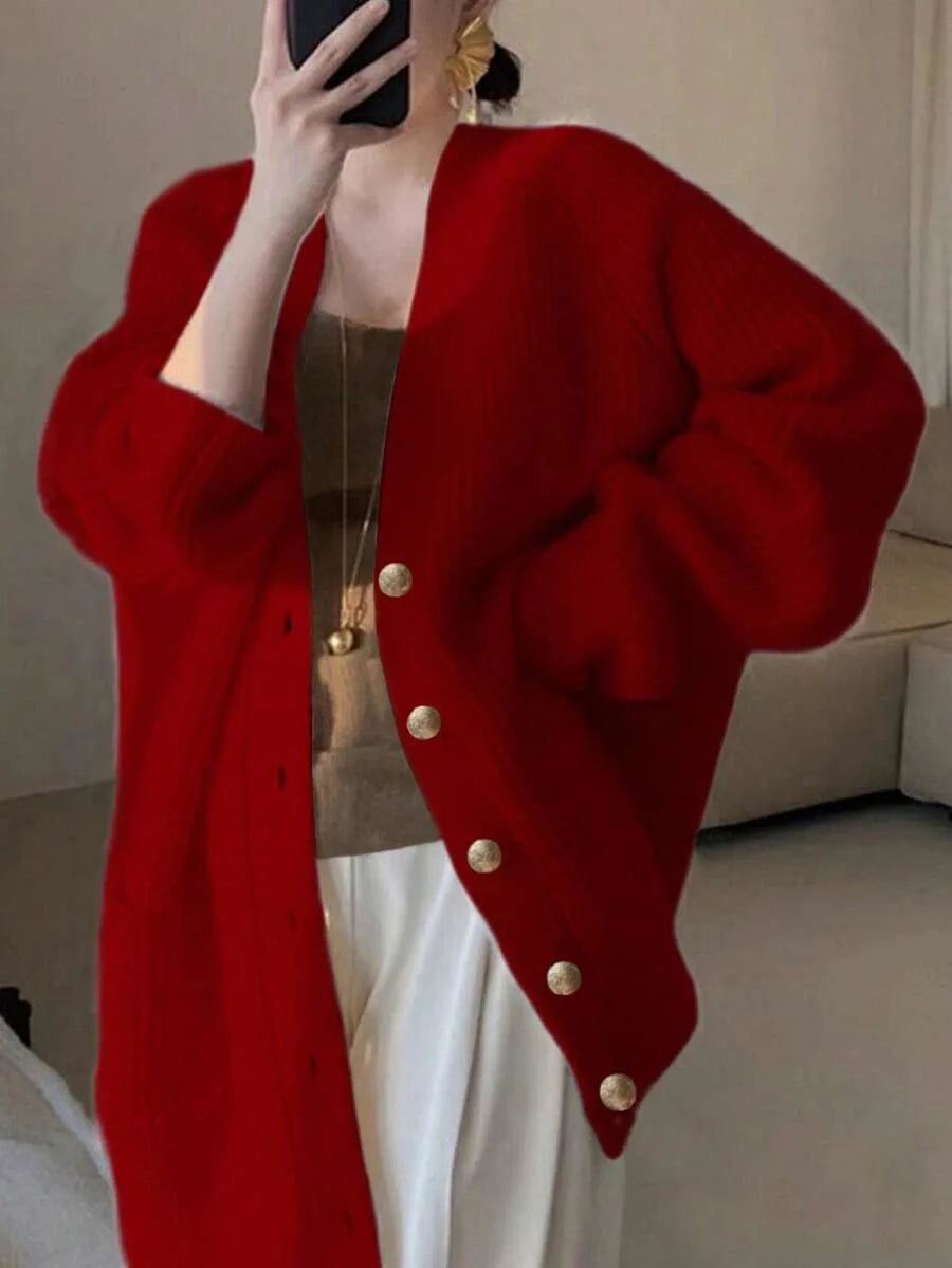 A woman wears an oversized red knit cardigan with gold buttons, holding a phone up to take a mirror selfie.