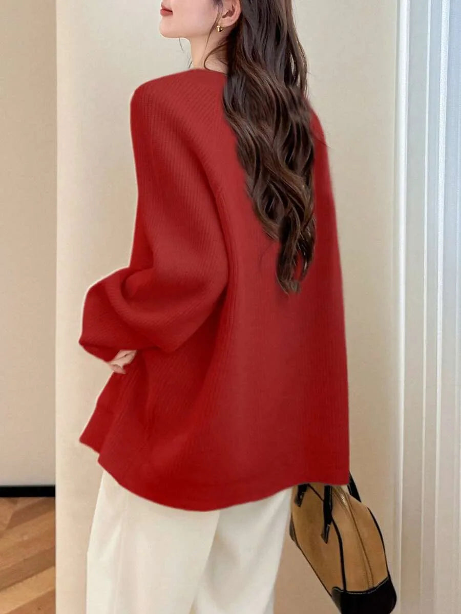 A woman seen from the back wearing an oversized red ribbed knit cardigan with white wide leg trousers, carrying a brown suede handbag.