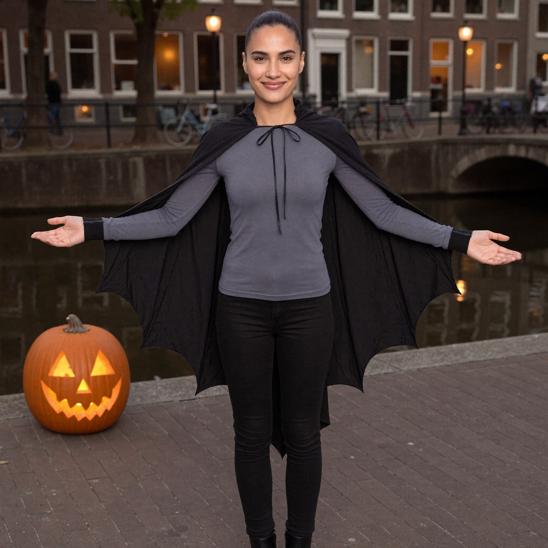 Vrouw in de zwarte vleermuiscape met strikkoord aan een Amsterdamse gracht met een Halloweenpompoen