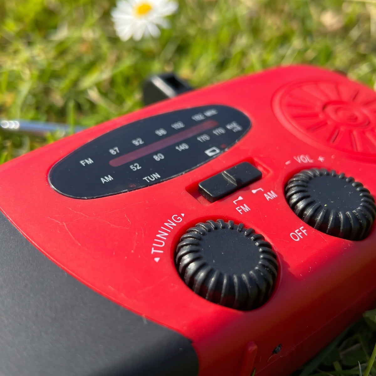 Rode noodradio met draaiknoppen buiten op gras gefotografeerd | Boutique Moda