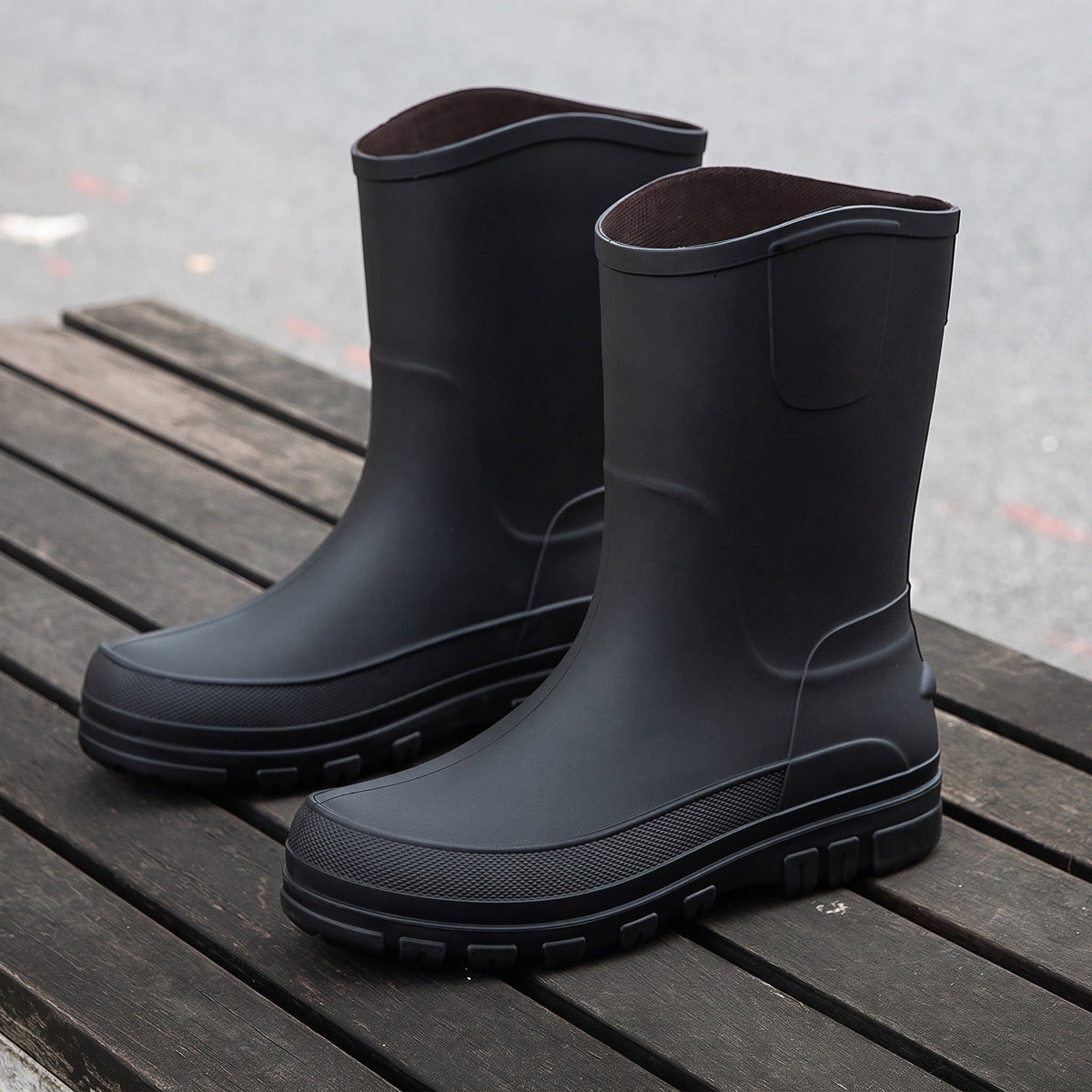 Zwarte halfhoge regenlaarzen met geribbelde zool, los staand op houten plank | Boutique Moda