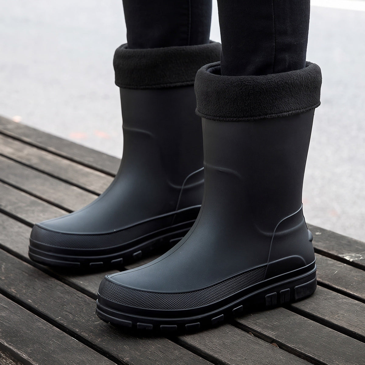 Zwarte halfhoge regenlaarzen met fleecemanchet, gedragen door een persoon op houten vlonder | Boutique Moda