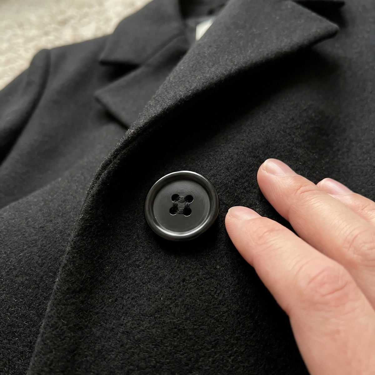 Zwarte dubbelrijige jas met grote knoop, close-up gedragen detail | Boutique Moda