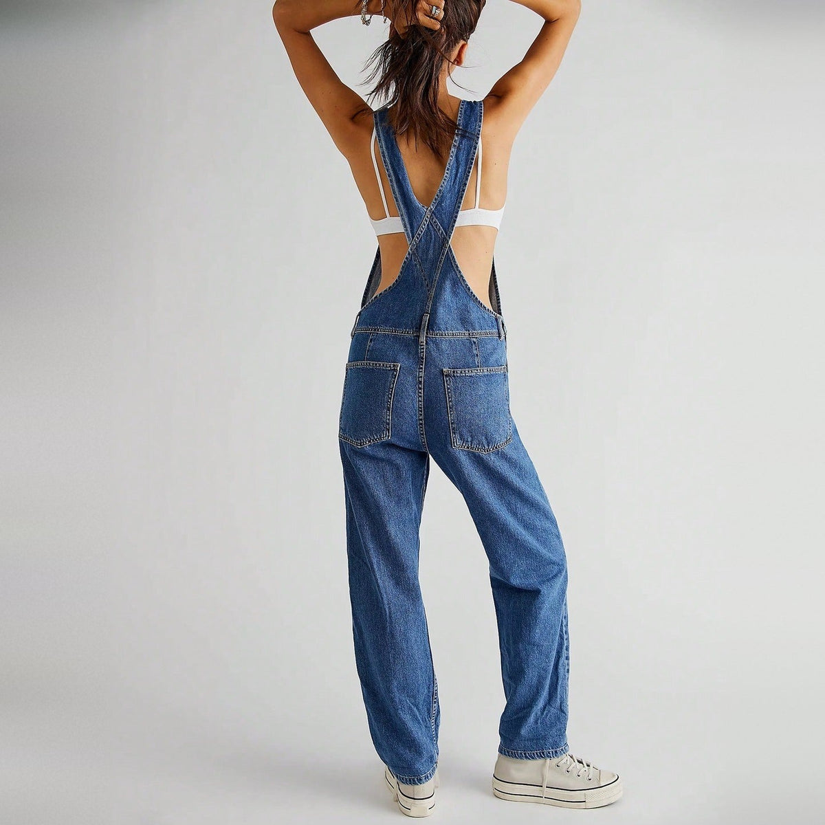 Blauwe denim tuinbroek met kruisbandjes, gedragen door vrouw met sneakers | Boutique Moda