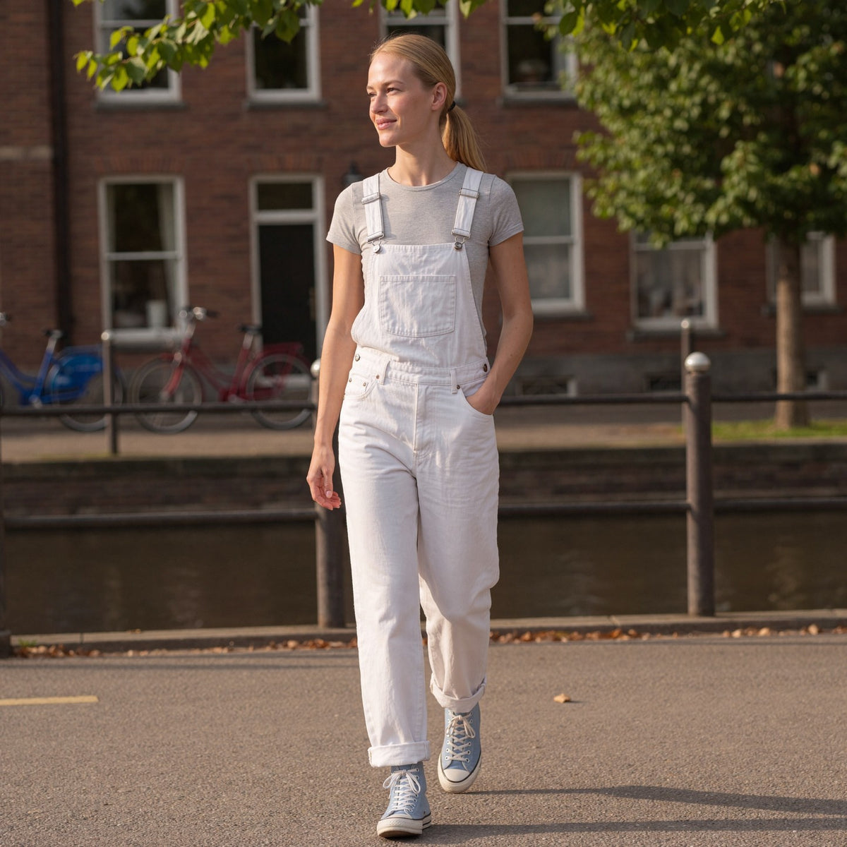 Vrouw draagt witte denim tuinbroek met grijs T-shirt langs een gracht | Boutique Moda