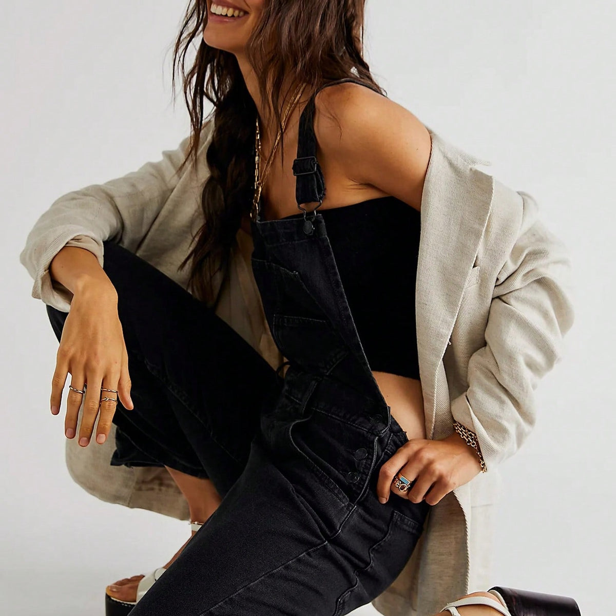 Vrouw draagt zwarte spijkerdungarees met beige oversized blazer, zittend | Boutique Moda