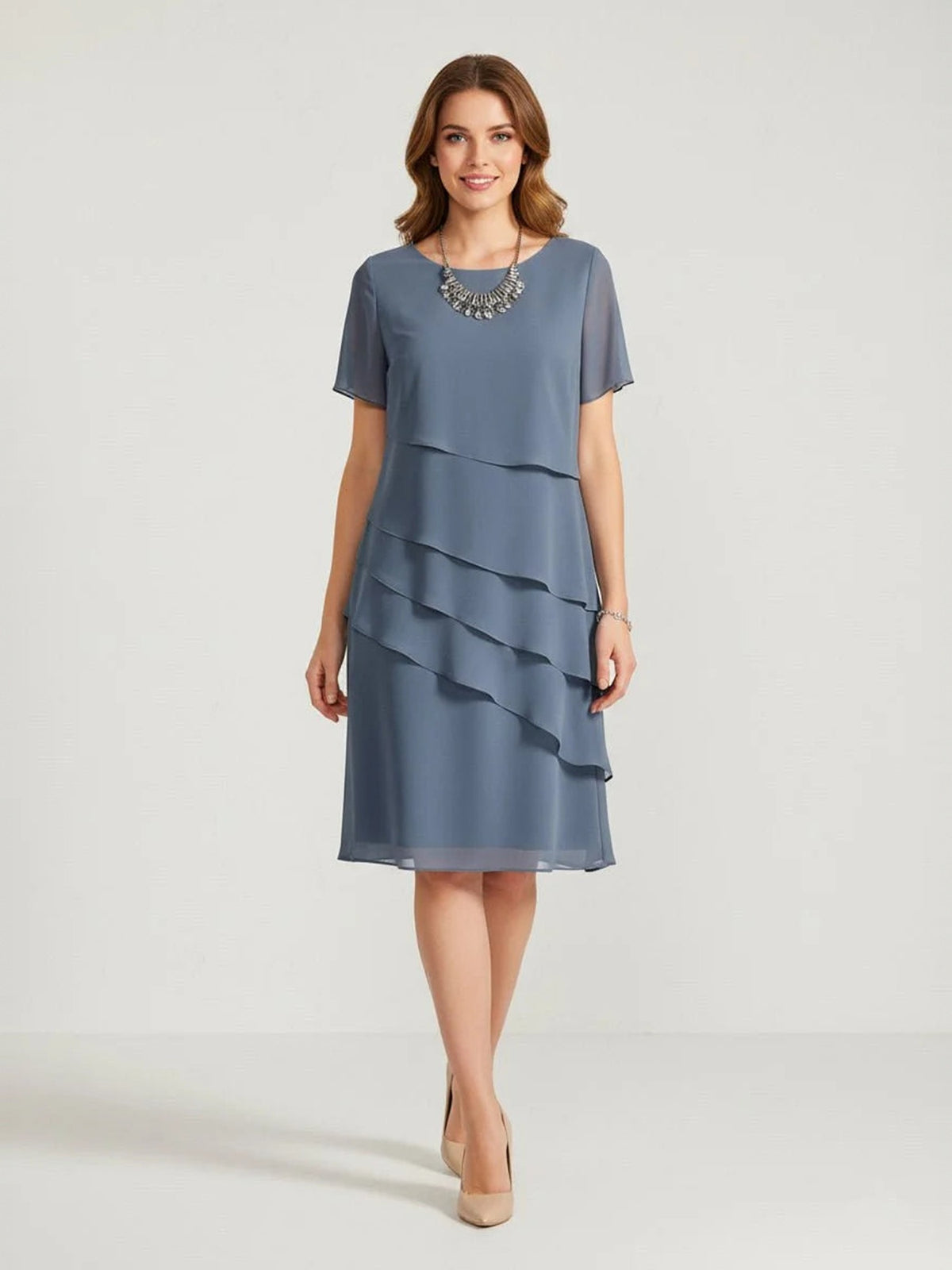 Blauwgrijze gelaagde chiffon jurk met korte mouwen, gedragen door model met ketting | Boutique Moda