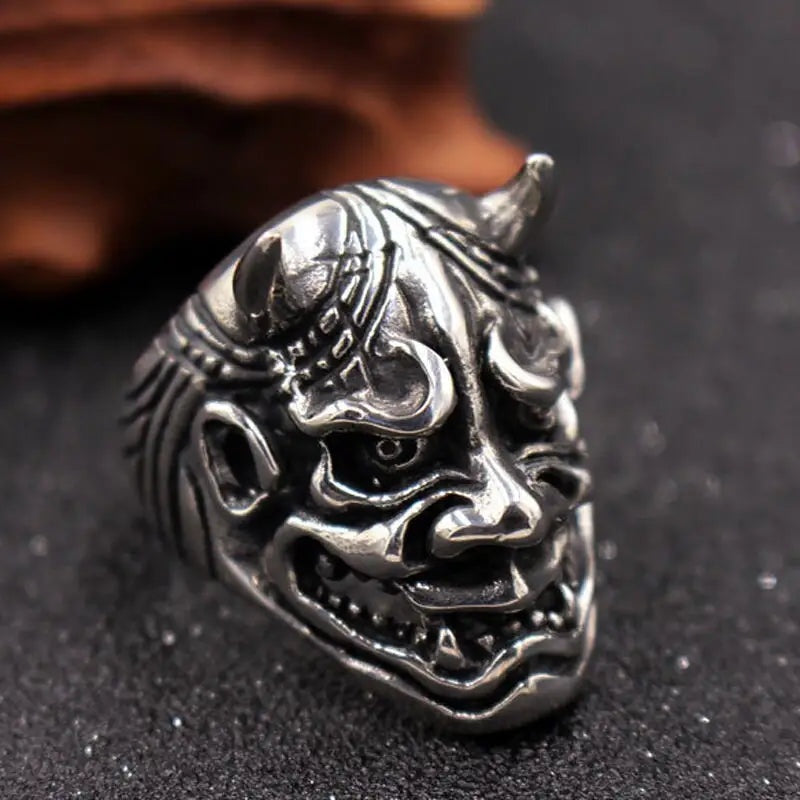 Zilverkleurige ring met gedetailleerd Oni-demonenmasker en hoorns, liggend op steen | Boutique Moda