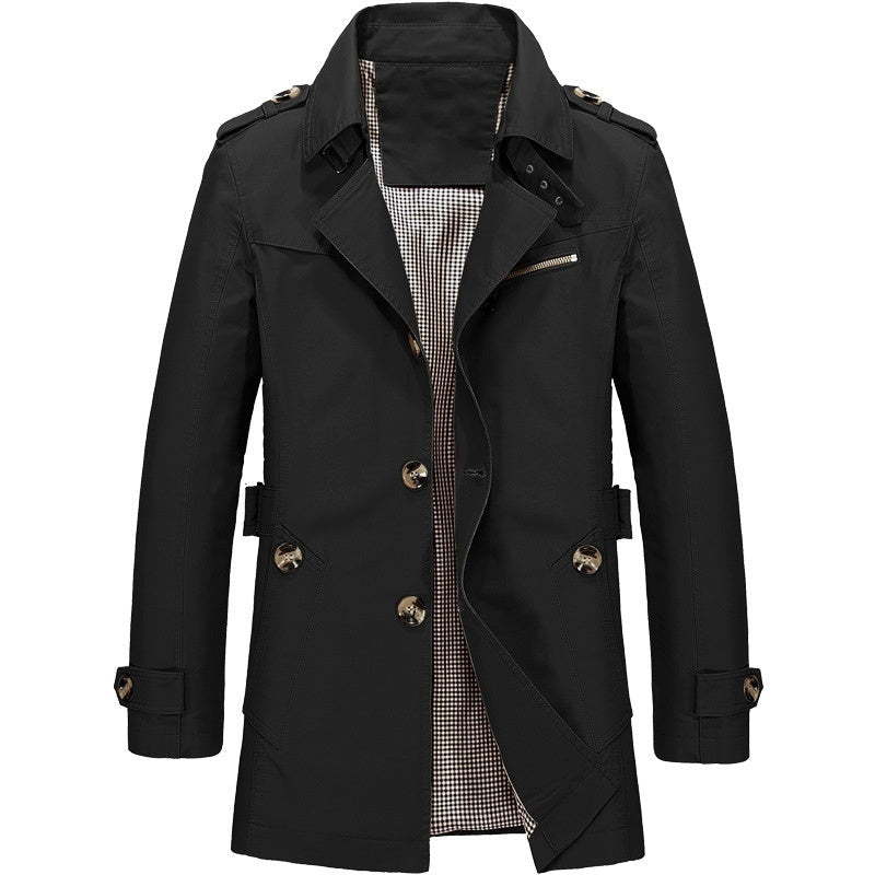 Zwarte trenchcoat met epauletten en knoopsluiting, geplooid op lichtgekleurde achtergrond | Boutique Moda