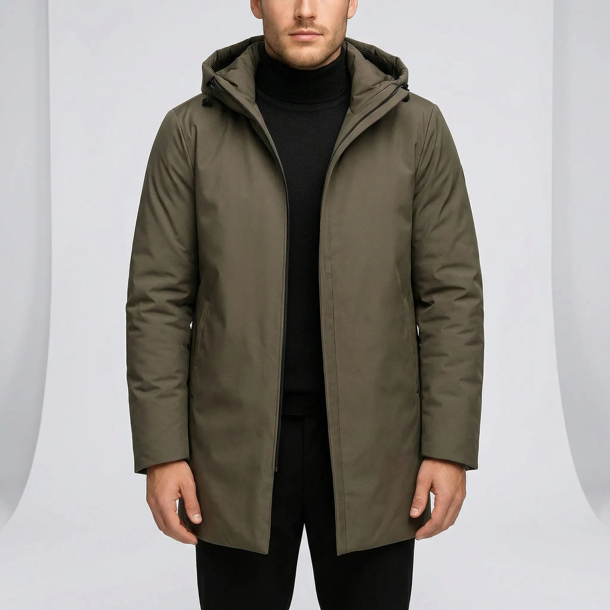 Man draagt effen groene regenmantel met capuchon, gefotografeerd met zwarte coltrui | Boutique Moda